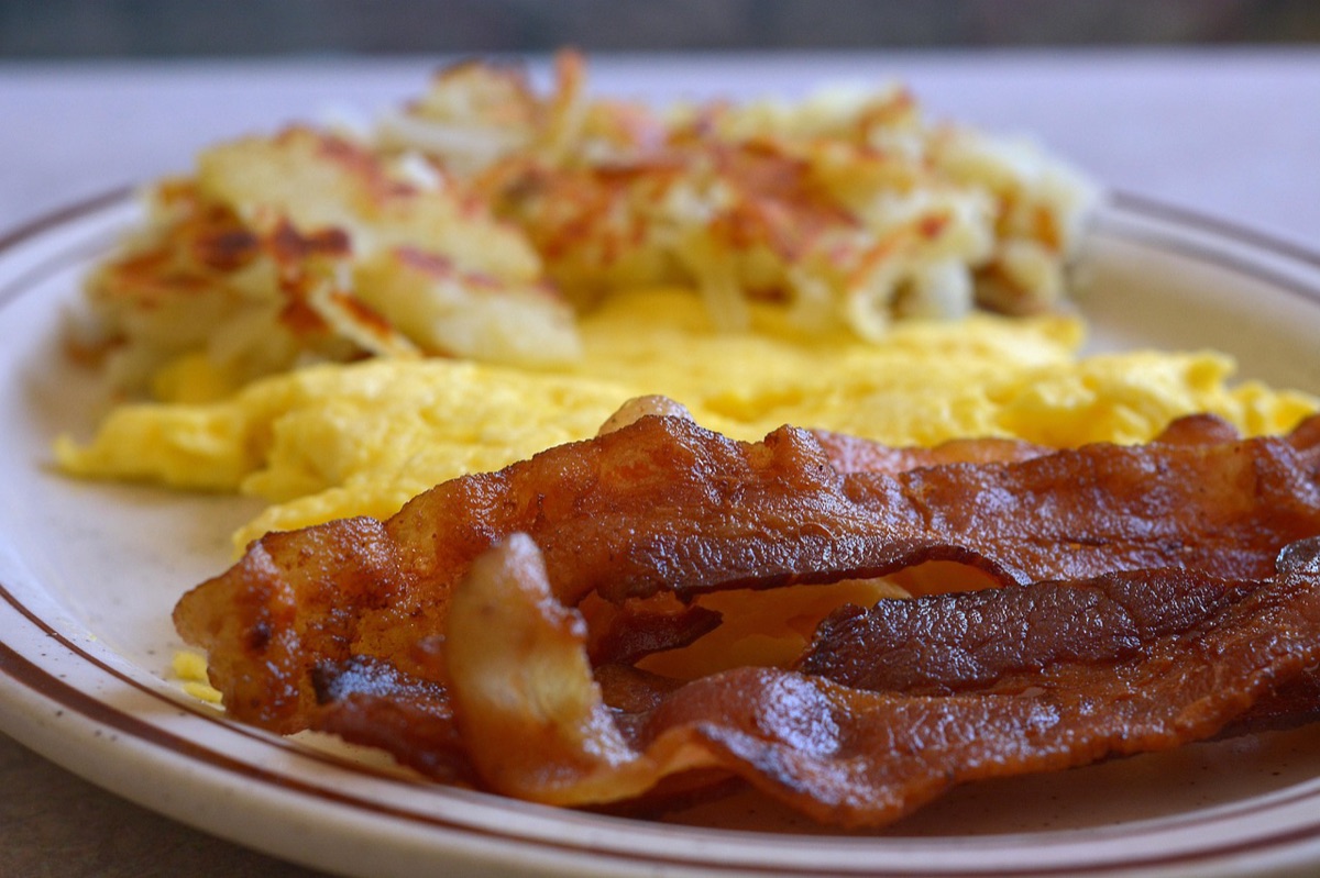 Huevos y bacon cocinándose en una pequeña sartén sobre una fogata de campamento.