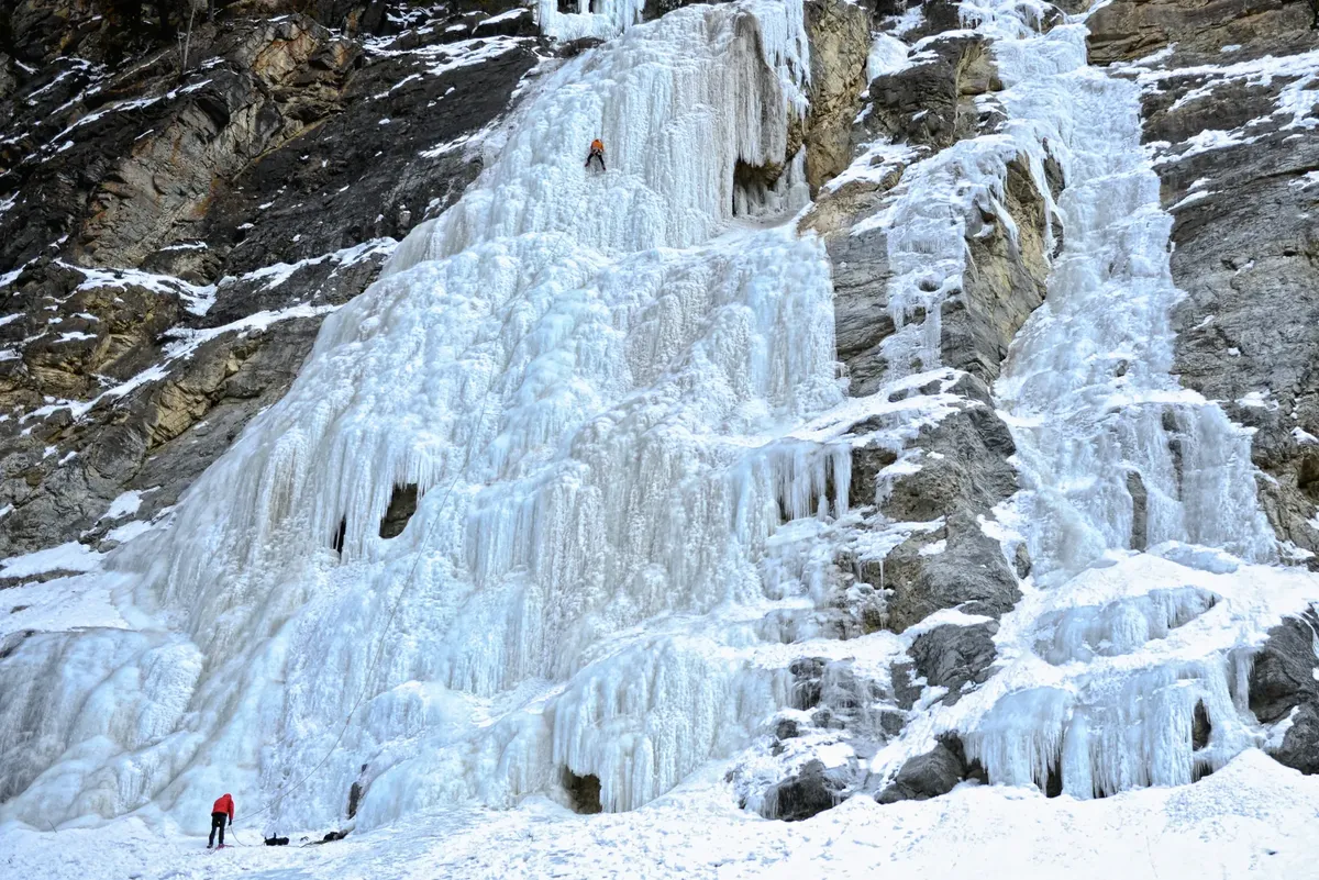Adventurous ice climbers challenge a towering frozen waterfall on a rugged mountainside in winter.