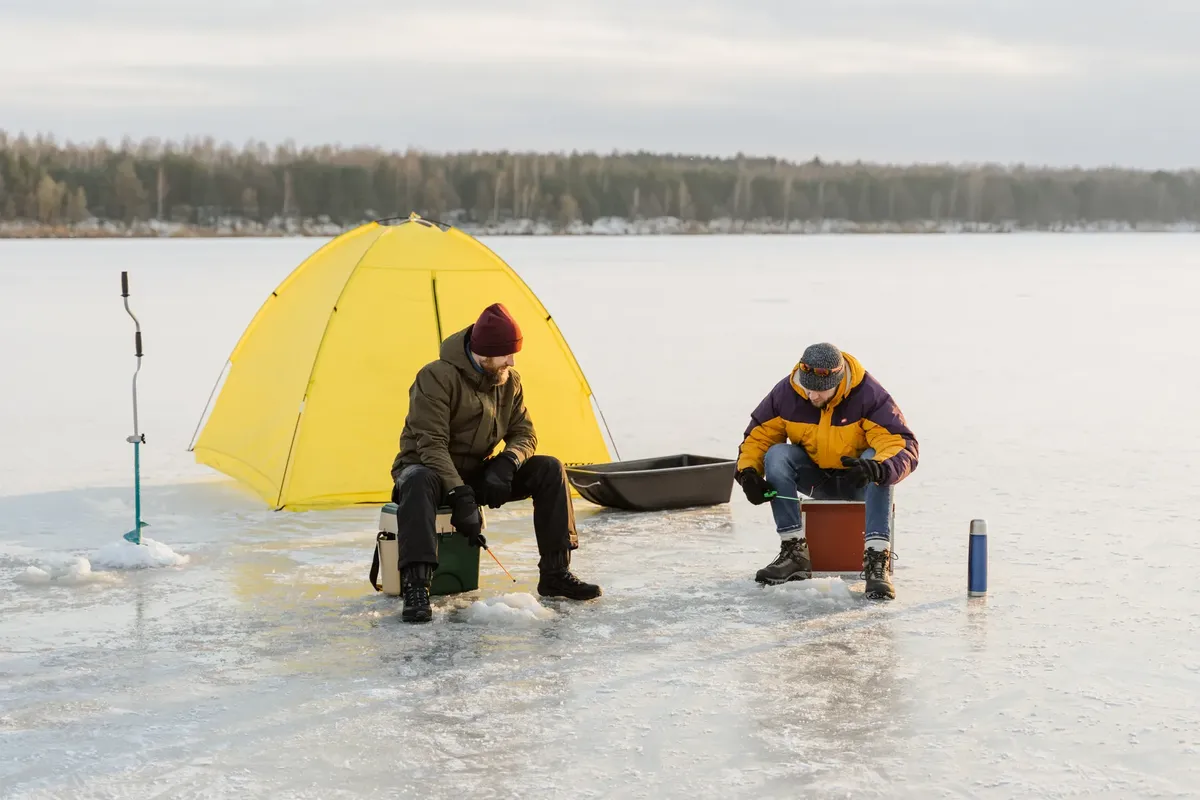 Two men ice fishing beside a yellow tent on a frozen lake, capturing the essence of winter leisure.