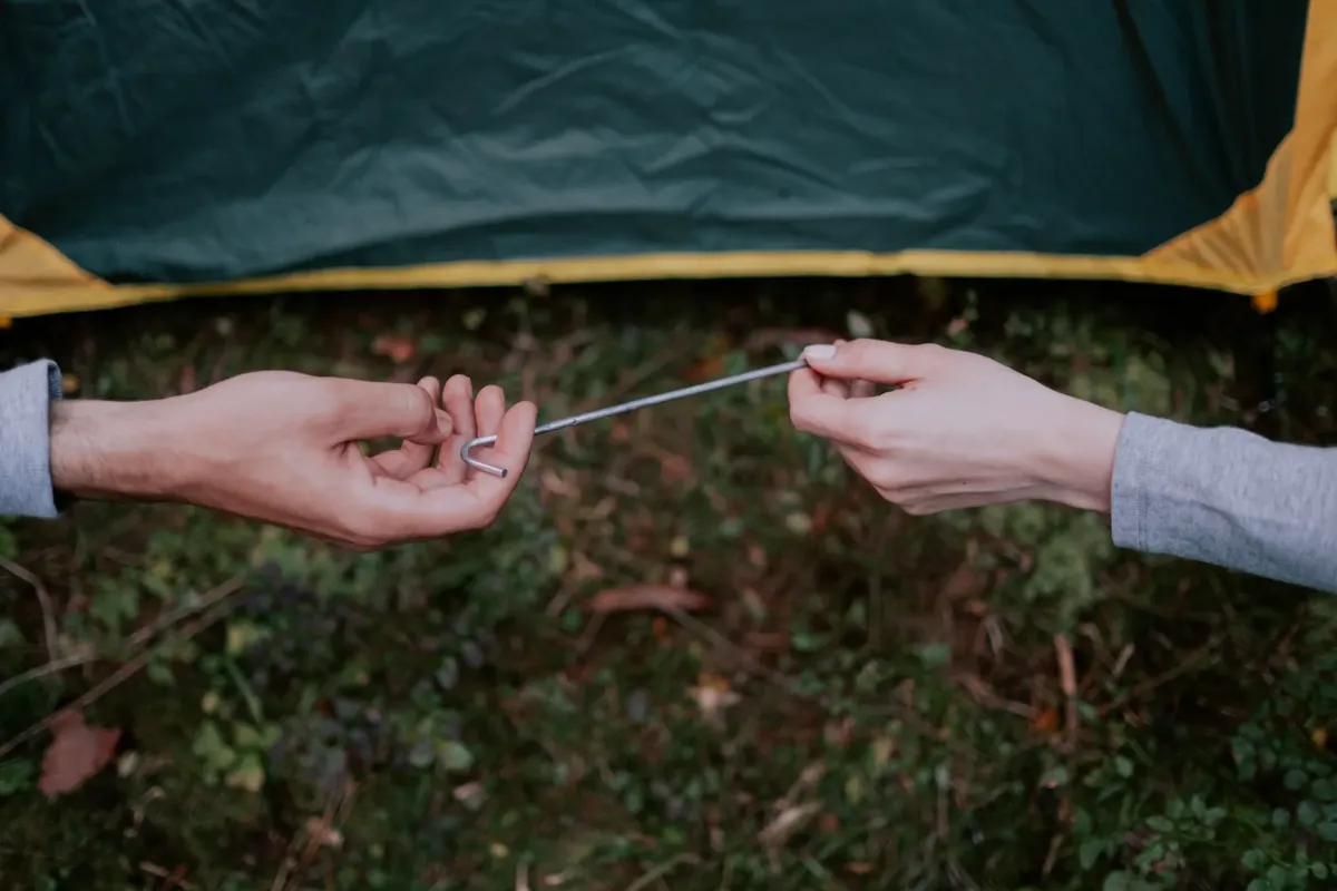 Two people setting up a tent using metal pegs in an outdoor camping area.