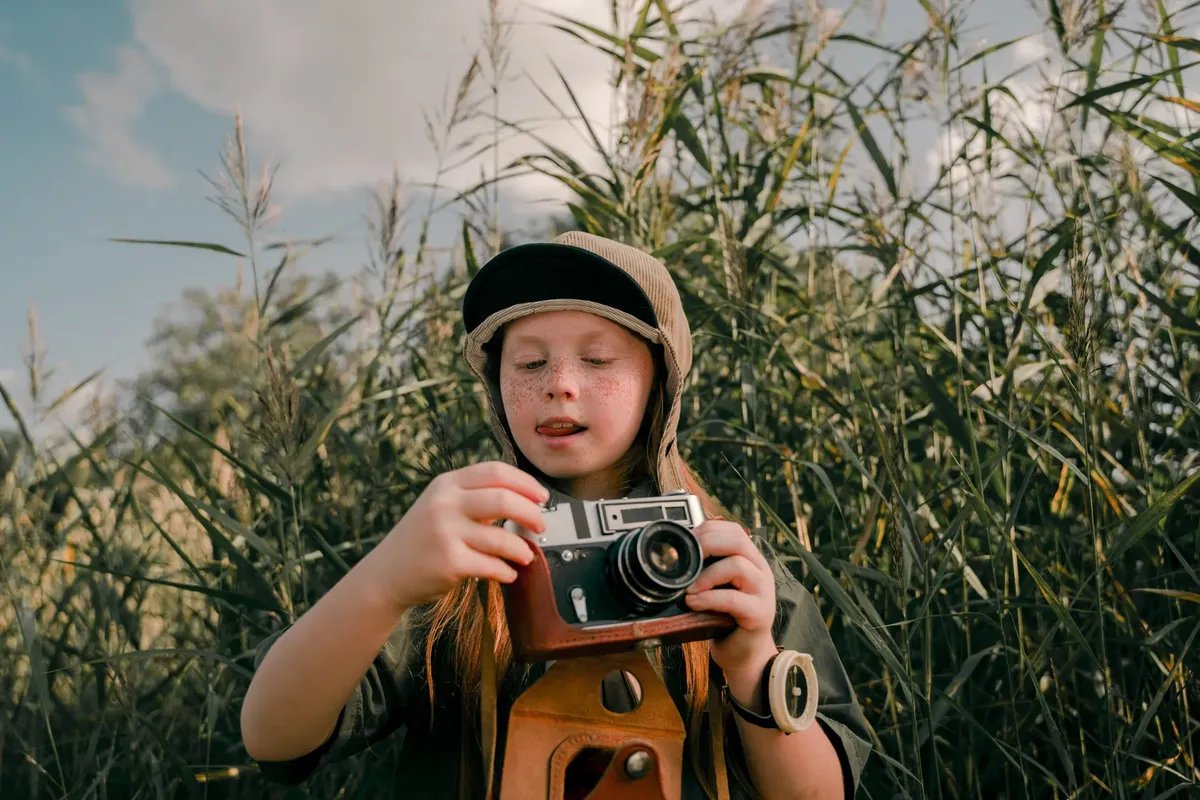 A child enjoying the outdoors with a vintage camera during a summer camp.