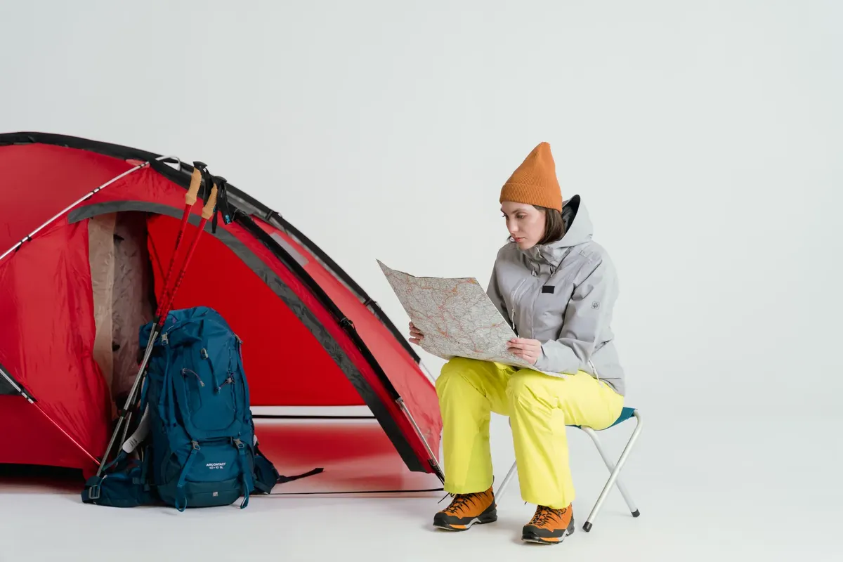 Woman in winter attire planning a camping trip with a map near a red tent.