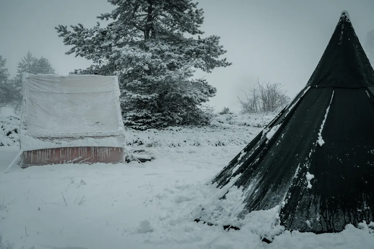 Snow-covered tents in a winter landscape, showcasing a serene and chilly outdoor camping scene.