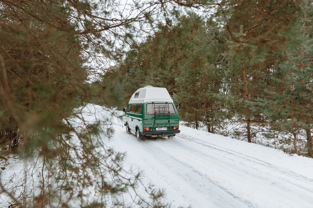 Green camper van driving on a snowy forest road during winter, capturing the spirit of adventure.