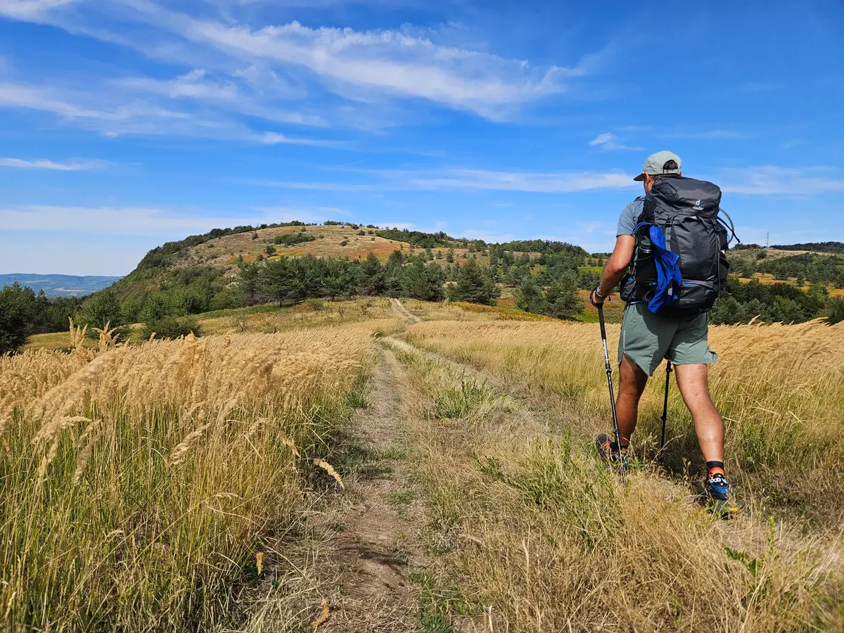 A hiker trekking along a scenic trail in the Balkan Mountains under a clear summer sky.