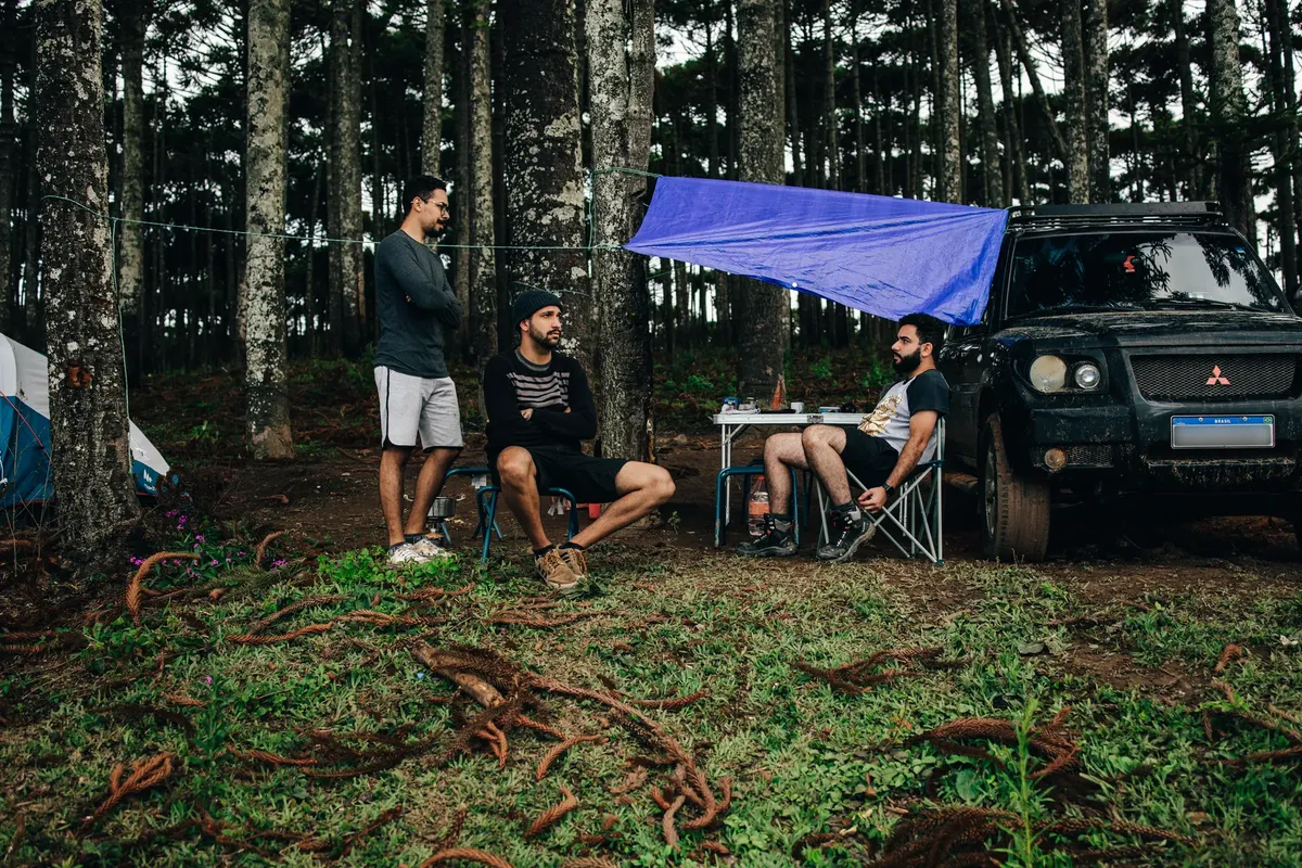 Three men camping in the forest with an SUV, tent, and folding chairs.